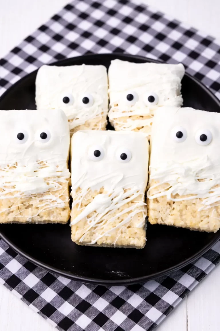 Halloween mummy Rice Krispies treats with candy eyes and white chocolate drizzle on a black plate