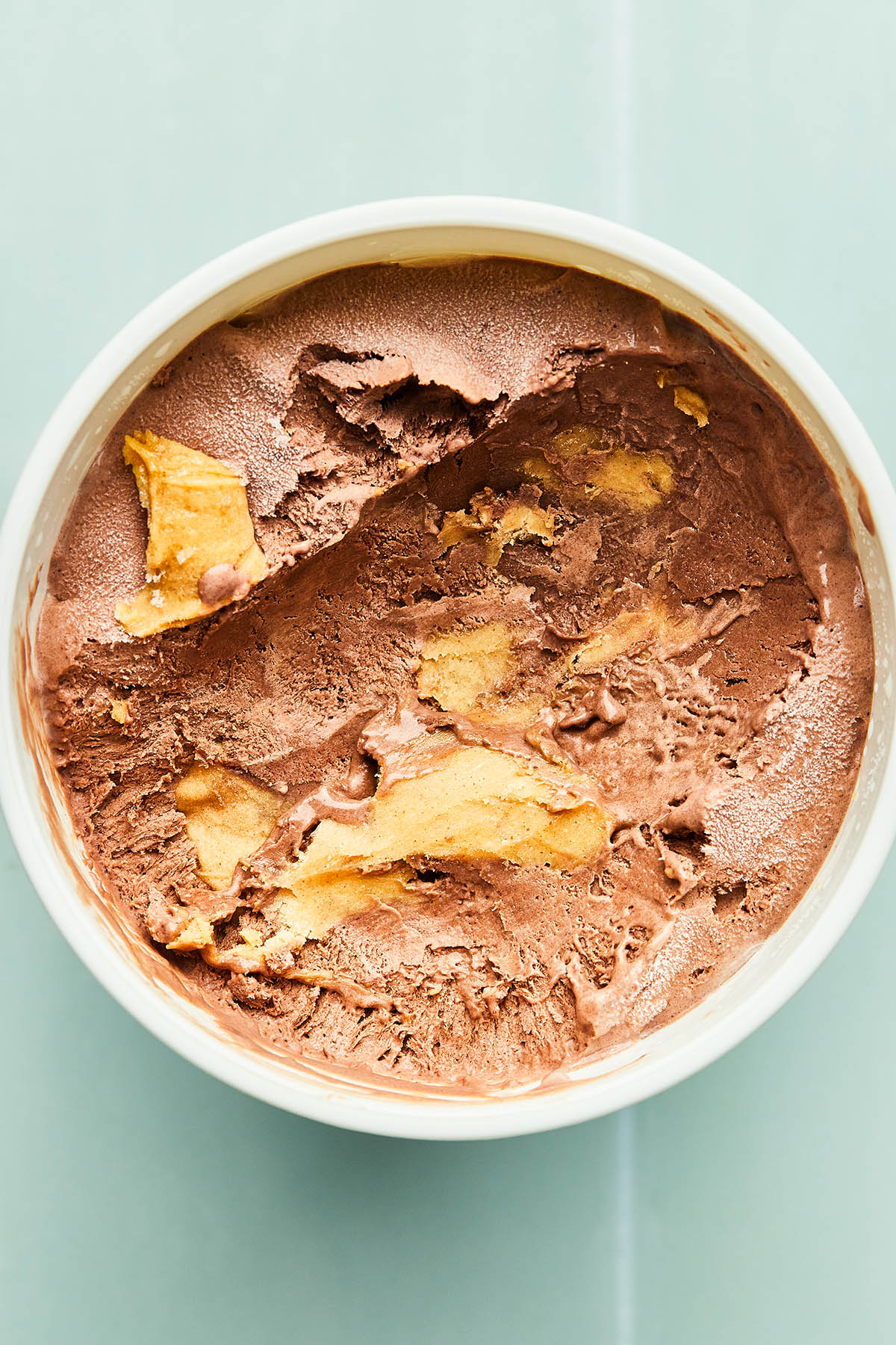 Chocolate peanut butter ice cream in a white bowl on a teal counter top.