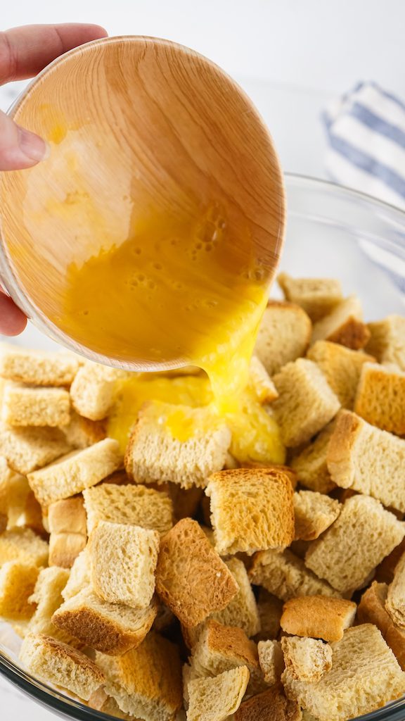 Adding the eggs to the sourdough bread cubes in a large mixing bowl.