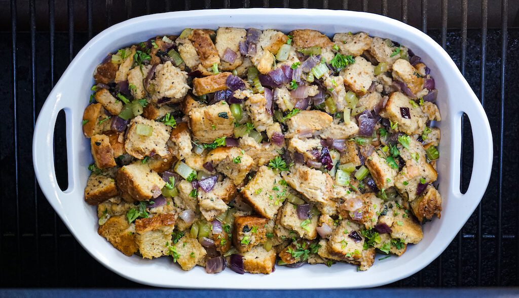 A white casserole dish full of smoked stuffing on a grill grate on the smoker.