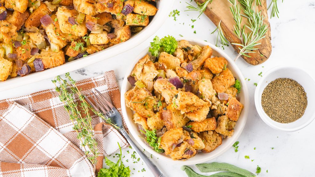 A bowl of smoked stuffing next to the casserole dish of stuffing with fresh herbs as an accent.