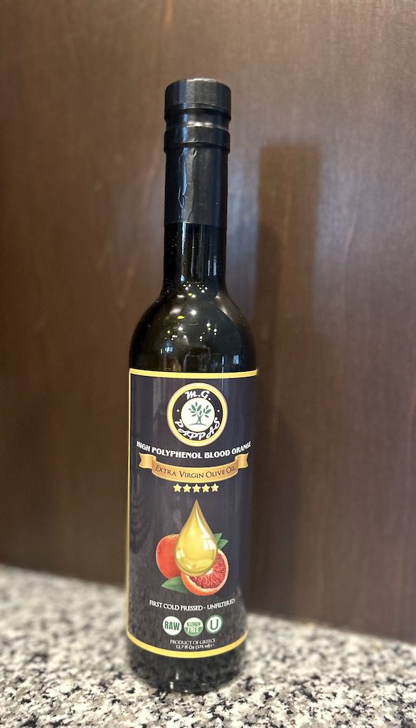 A bottle of blood orange olive oil on a granite counter with a wooden background.