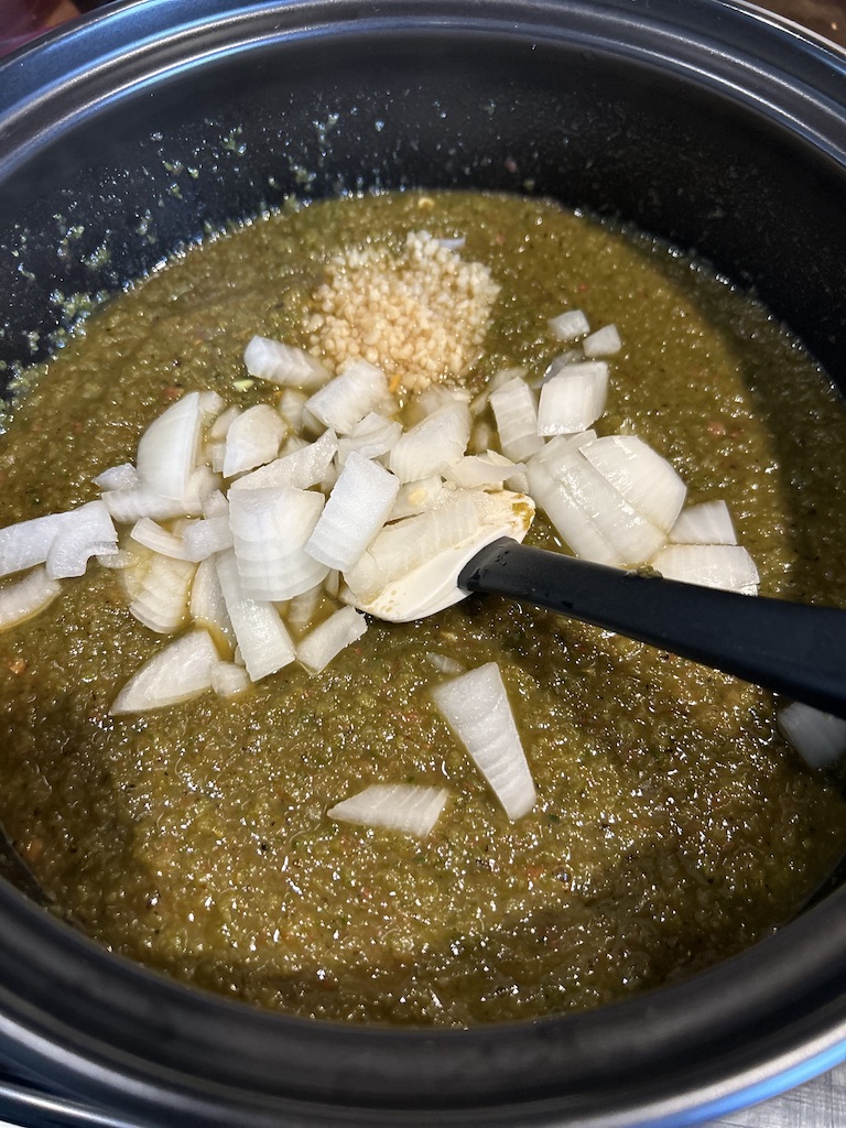 A large dutch oven pot filled with the smoked green chili sauce, diced onions and garlic.
