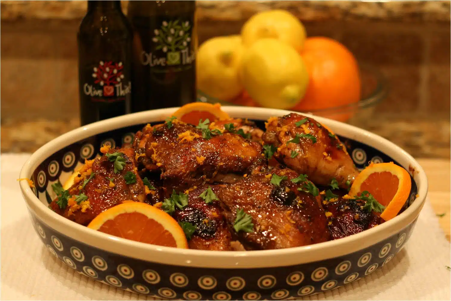 Baked orange-glazed chicken thighs with herbs and citrus slices in bowl