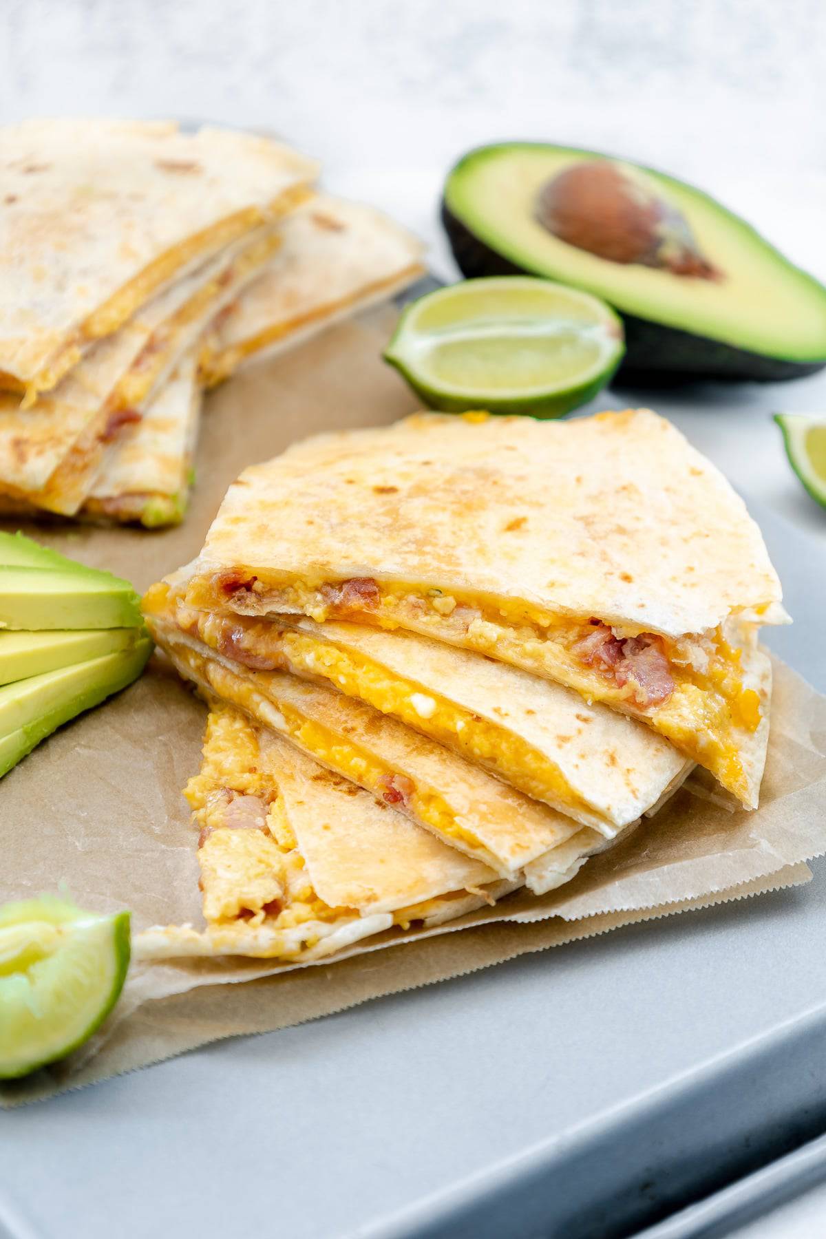 A breakfast quesadilla sliced on parchment paper with fresh lime wedges and halved avacados.