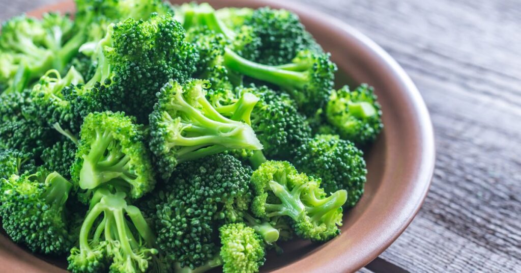 A bowl of broccoli florets in a brown bowl on a wooden counter.