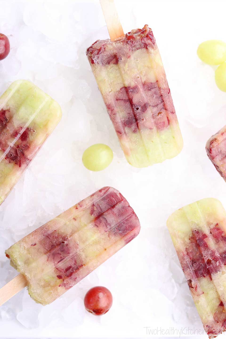 A selection of sugar free frozen grape popsicles on ice with a few whole grapes.
