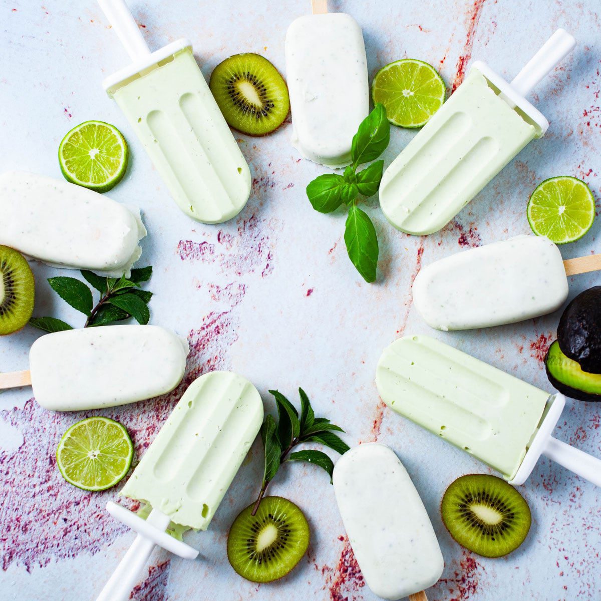 A circle of homemade sugar free popsicles with fresh kiwi and lime slices and mint leaves on a marbled background.