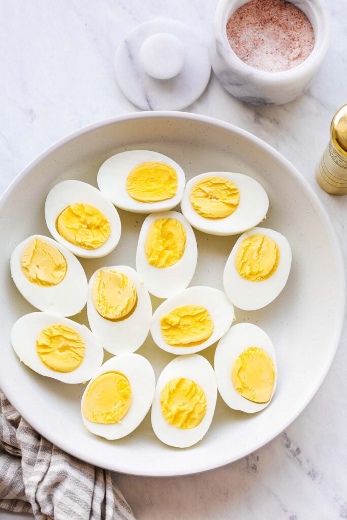 Halved hard-boiled eggs in a white bowl with pink salt on marble
