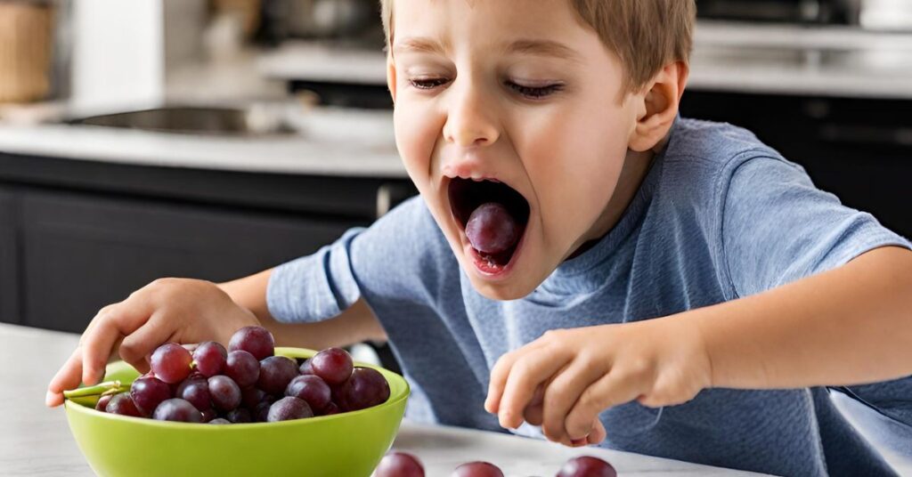 A boy eating grapes from a green bowl in the kitchen.