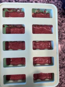 A popsicle mold half filled with mango cherry popsicle filling.