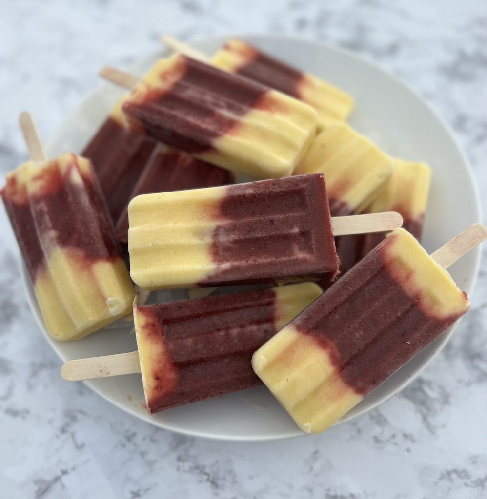 A white plate piled with cherry mango popsicles on a counter top.