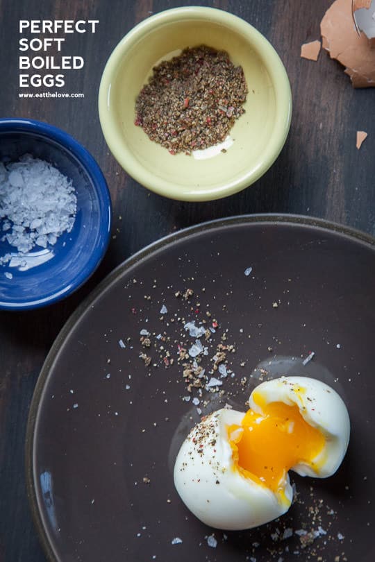 A perfectly soft boiled egg in a bowl with two bowls of fresh cracked black pepper and salt.