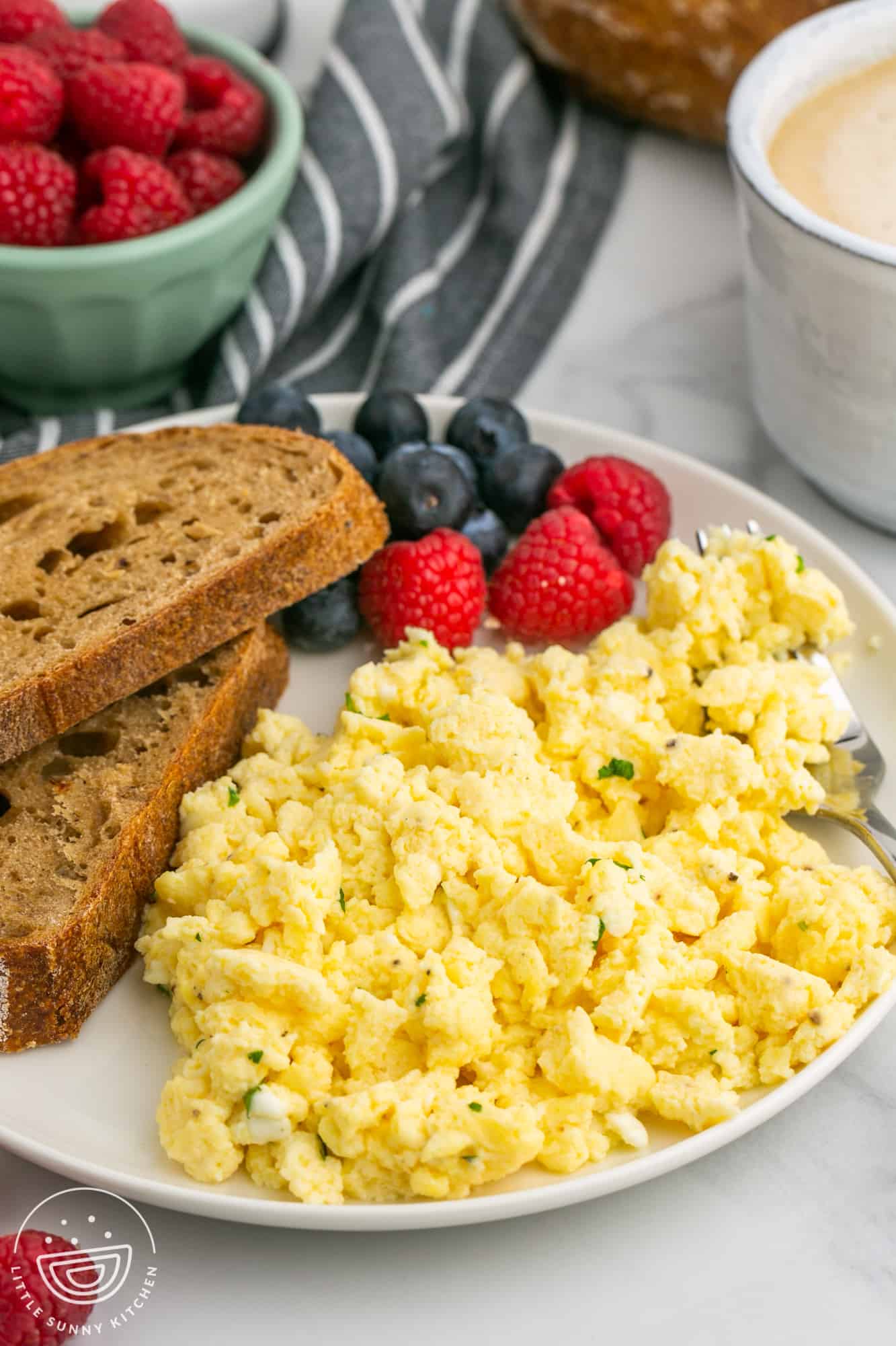 A white plate filled with scrambled eggs with cottage cheese with toast and fresh berries.