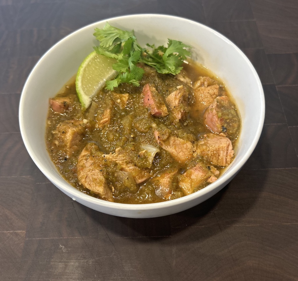 A white bowl of smoke chili verde with cilantro and lime garnishes.