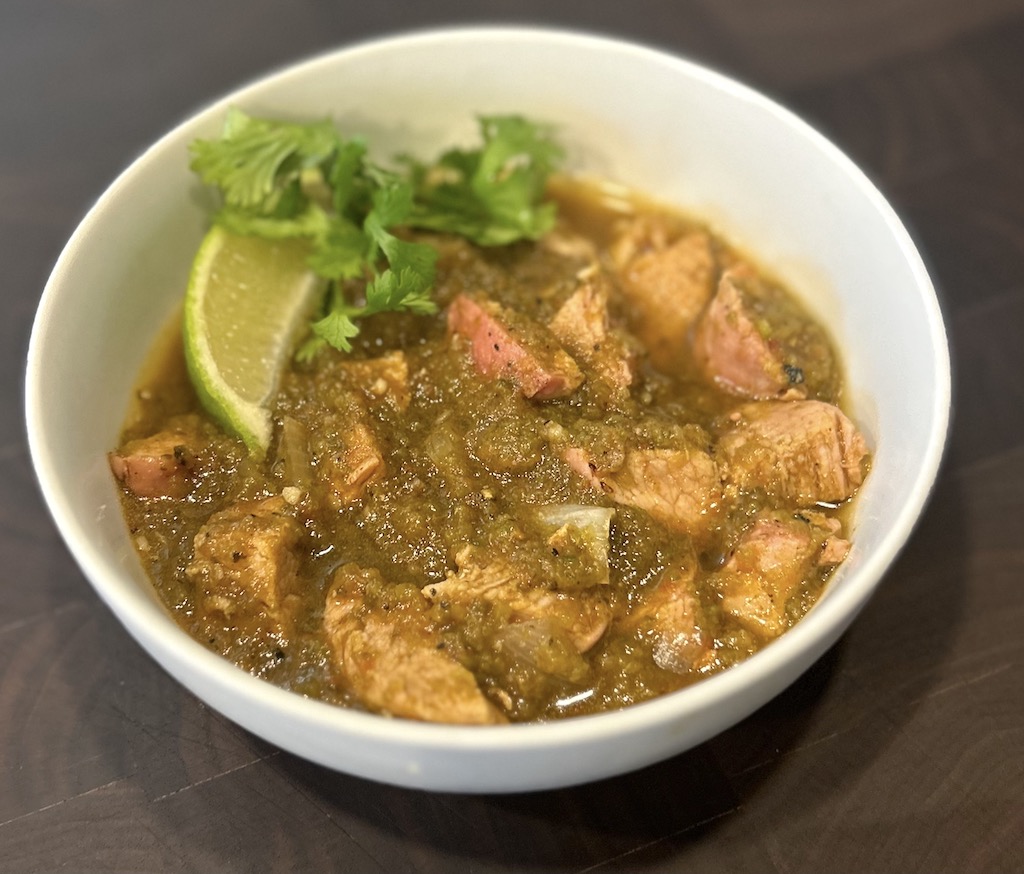 A bowl of smoked green chili with a garnish of fresh lime wedge and cilantro.