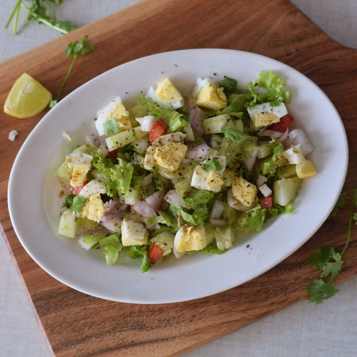 A white oval plate on a wooden cutting board featuring a chefs salad with hard boiled eggs.