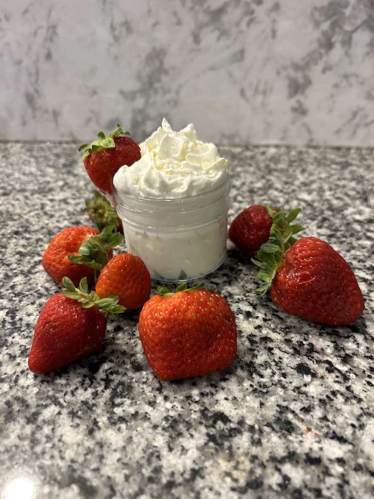 Whipped cream in a small mason jar on a granite counter top with fresh strawberries.