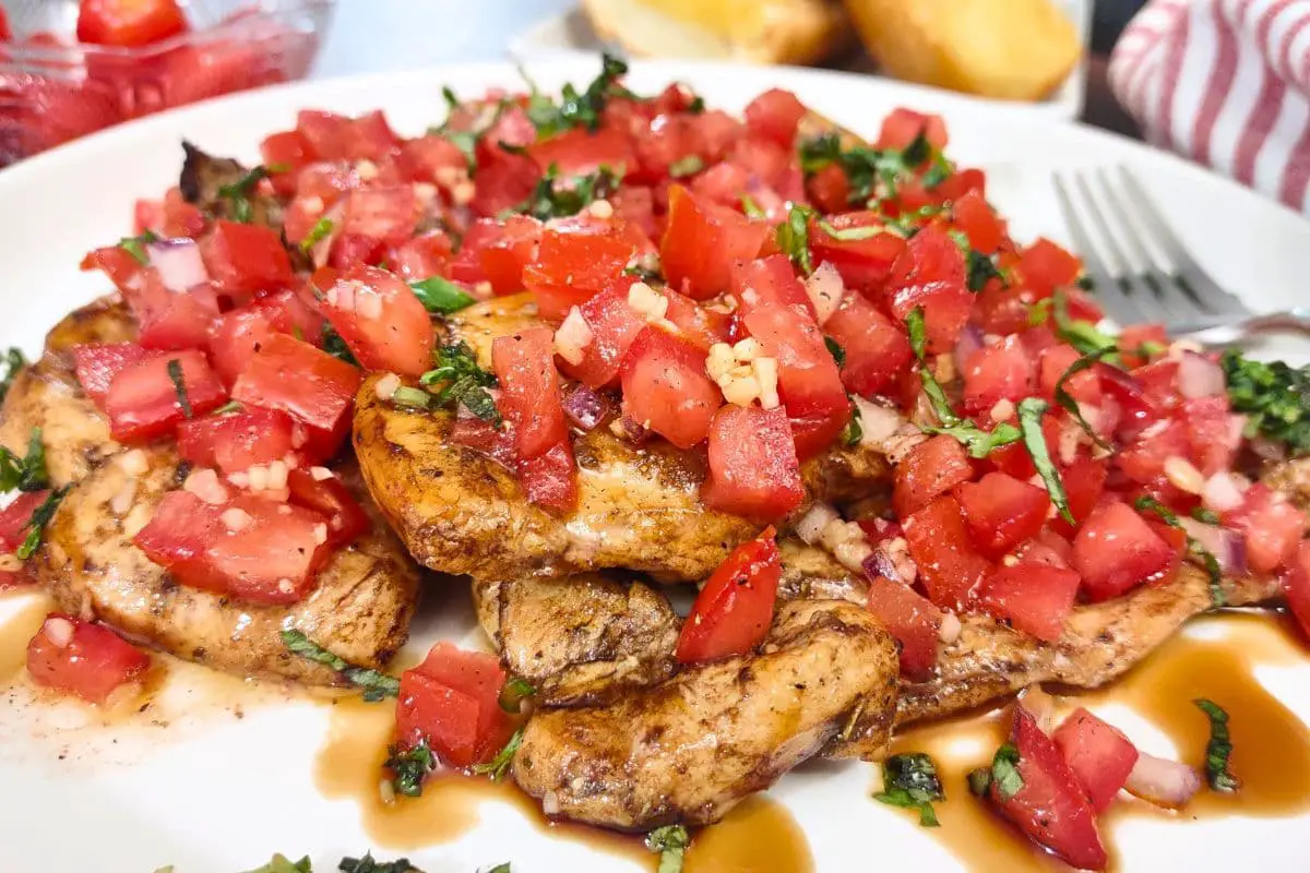 A white plate with a fork filled with air fryer brushetta chicken including a fresh tomatoes and garlic!