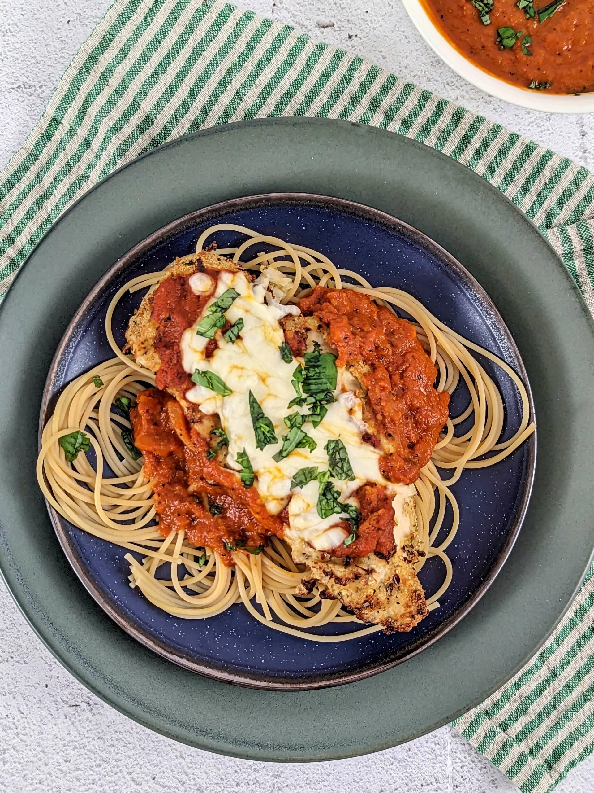 A blue and green plate on a green and beige stripped napkin full of air fryer chicken parmesan.