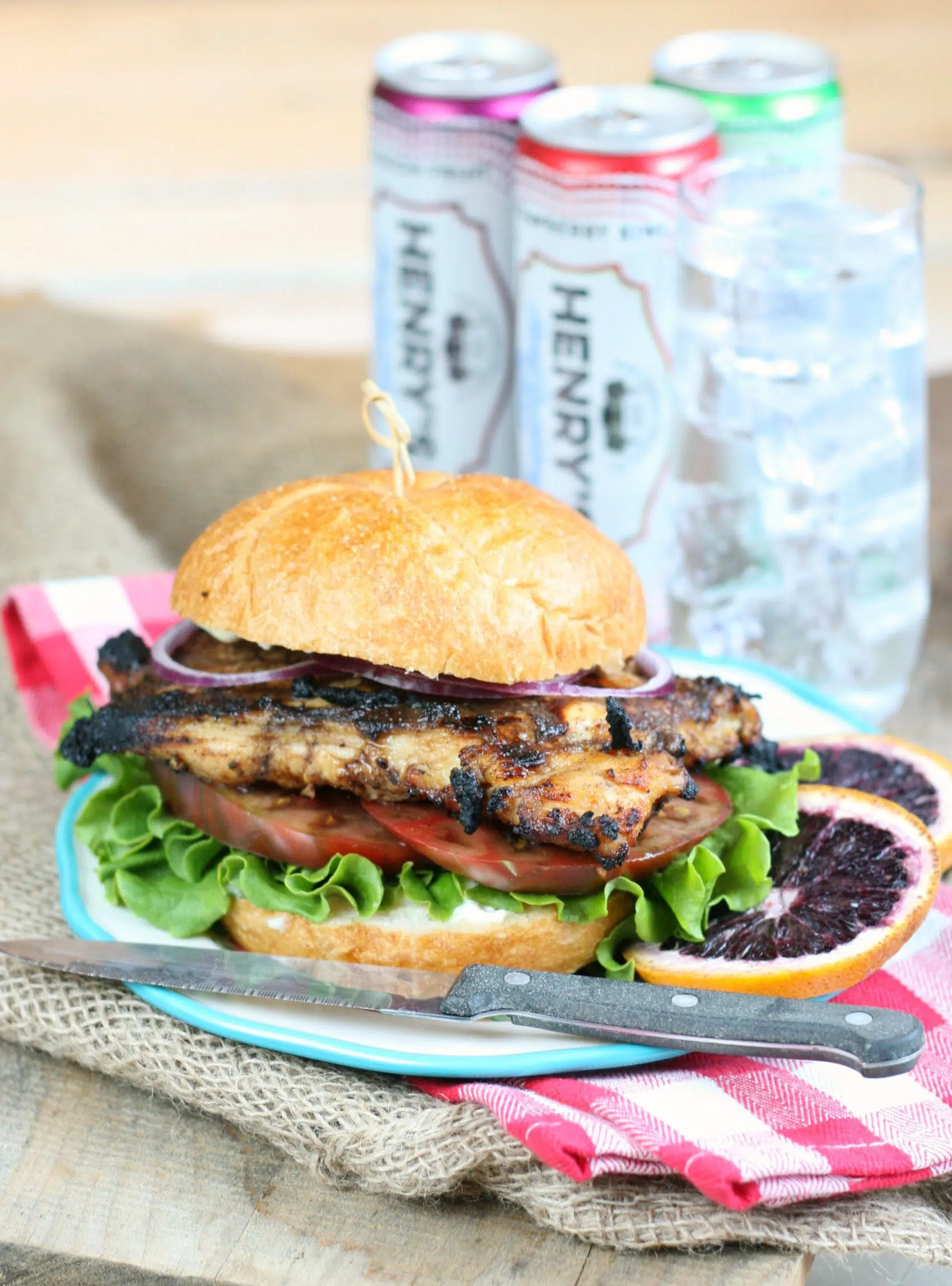 Grilled chicken sandwich with lettuce, tomato, and onion, with blood orange slices and soda cans