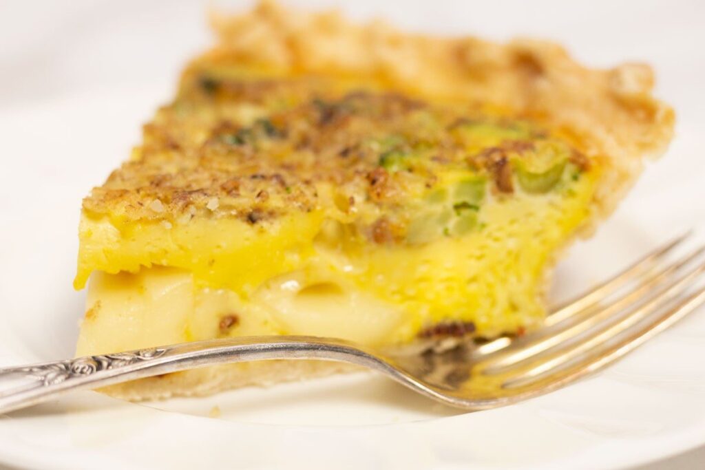 Close-up slice of vegetable quiche with cheese and fork on plate