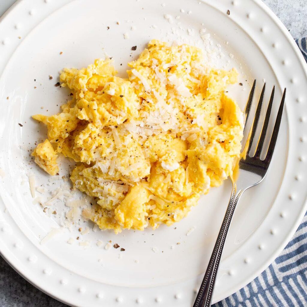 Creamy scrambled eggs with grated Parmesan and pepper on a white breakfast plate