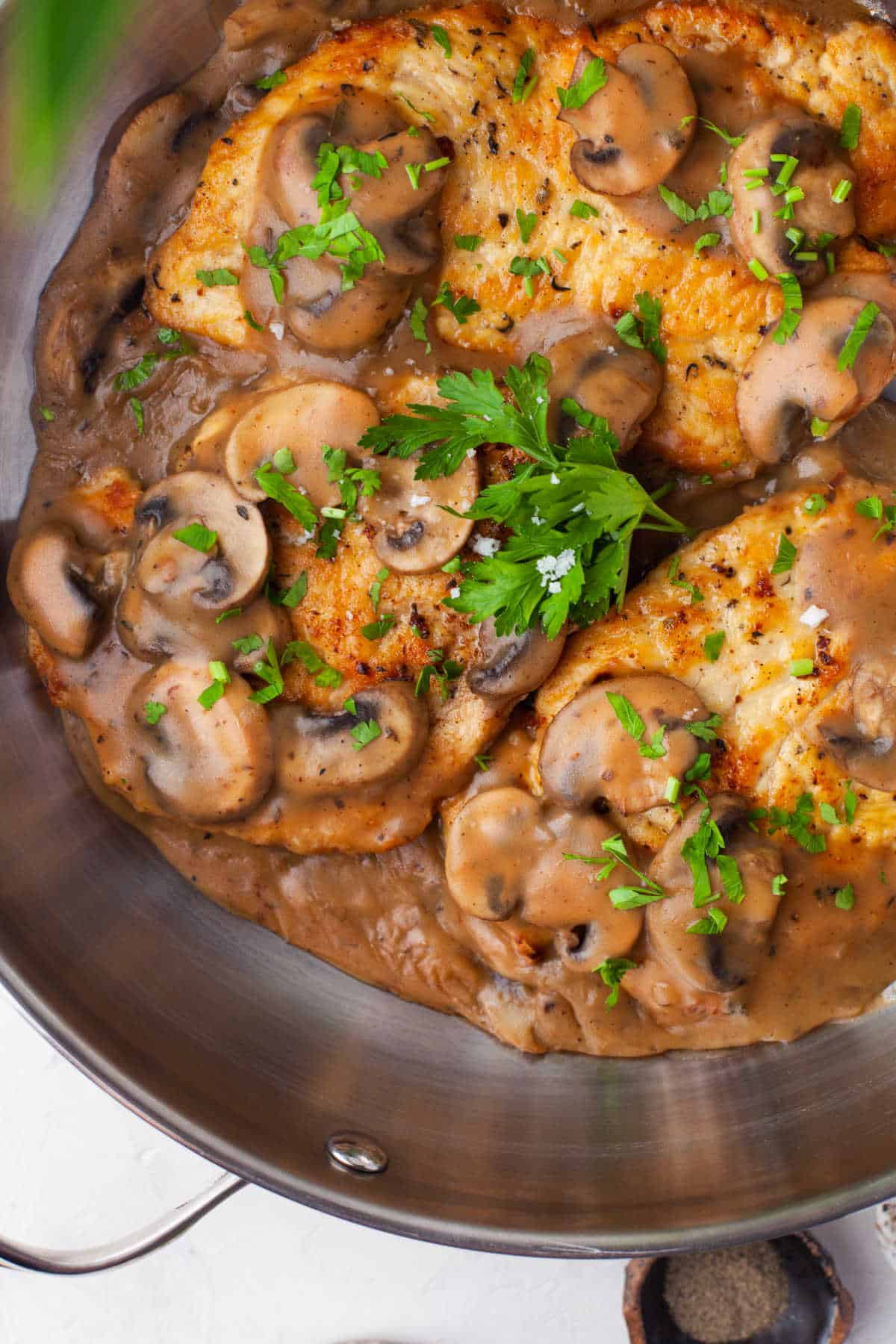 A pan filled with easy chicken marsala a recipe made with thinly sliced chicken breasts and mushrooms garnished with fresh parsley.
