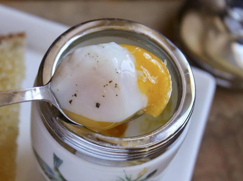 Spoon lifting coddled egg with runny yolk and pepper from egg coddler