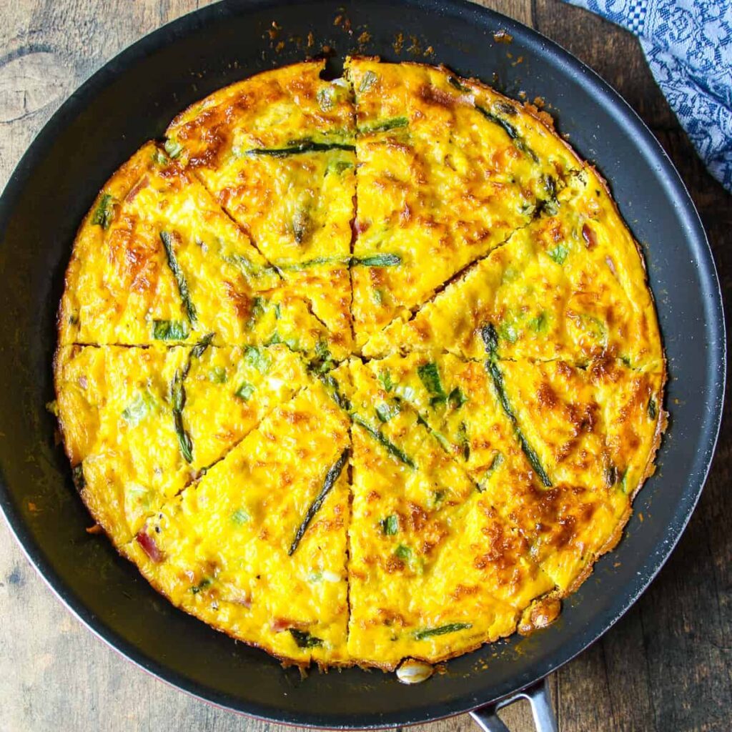 Golden-brown cheesy asparagus frittata in skillet, sliced wedges
