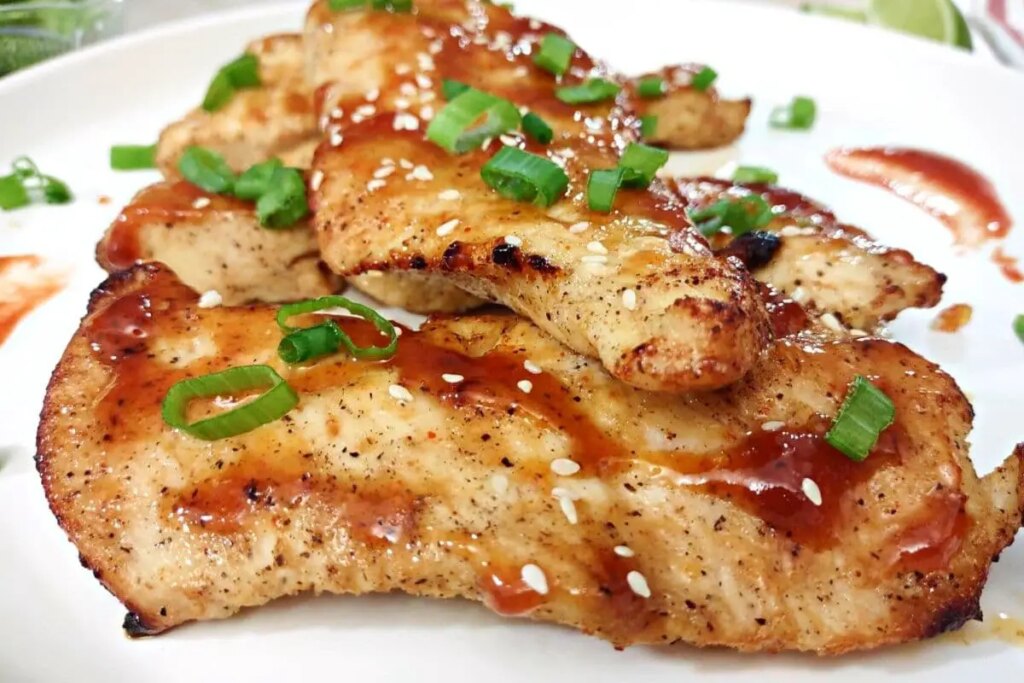 13 Recipes for Thinly Sliced Chicken Breasts A large white plate full of honey sriracha chicken garnished with fresh scallions.