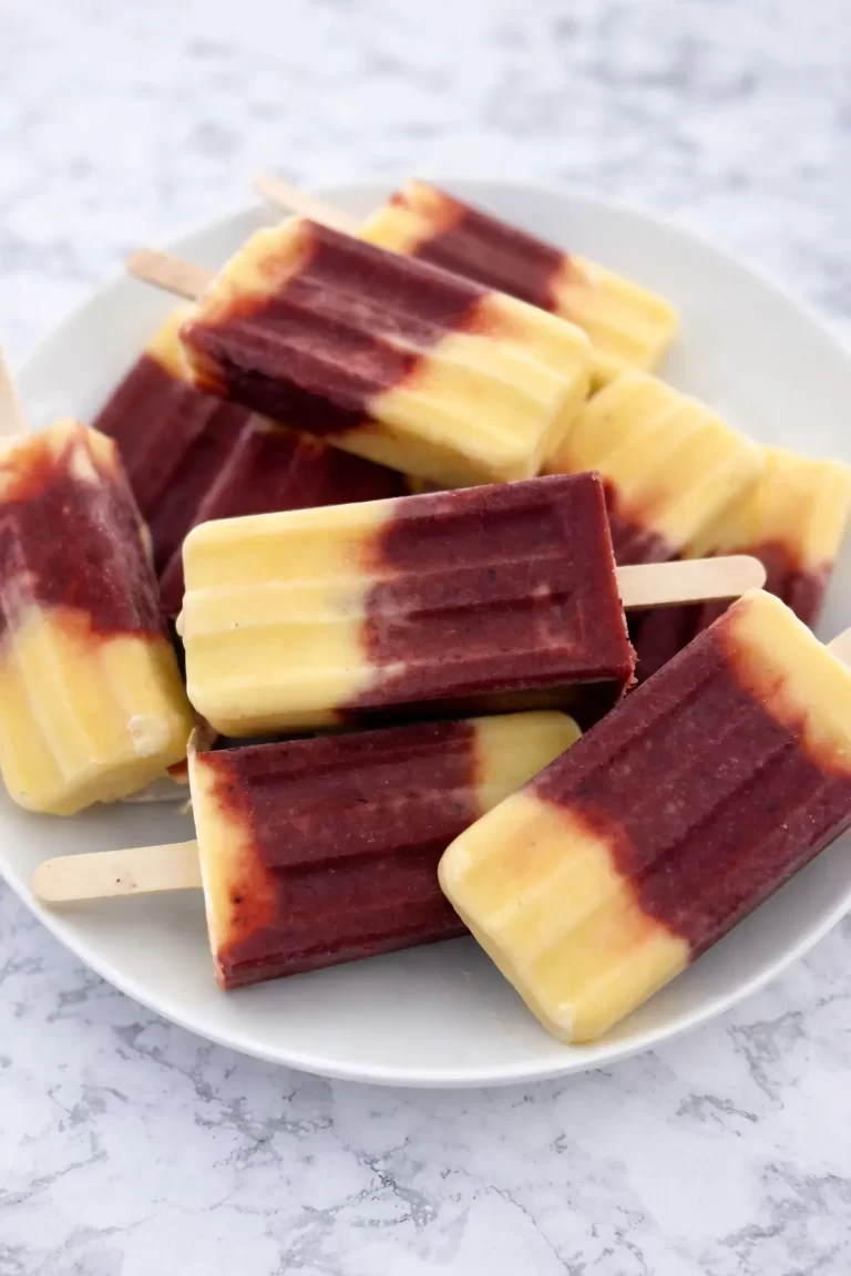 Stack of layered mango and berry popsicles on a white plate, summer frozen treats