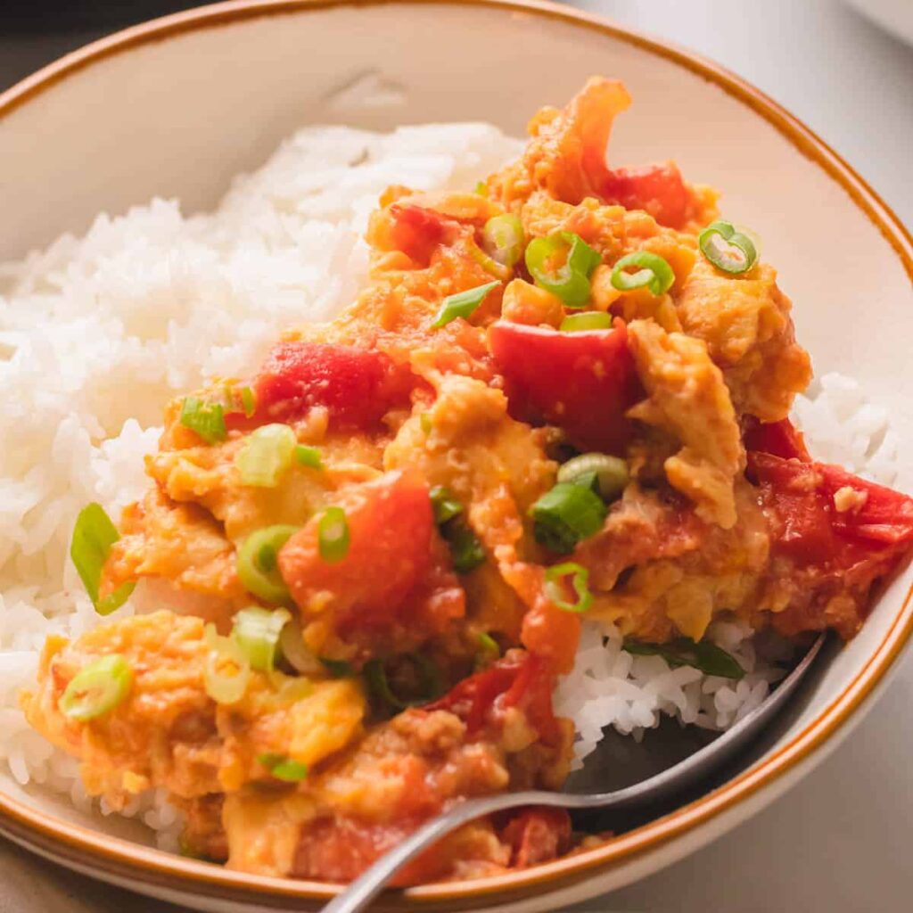 Tomato egg stir fry in a bowl on top of white rice.