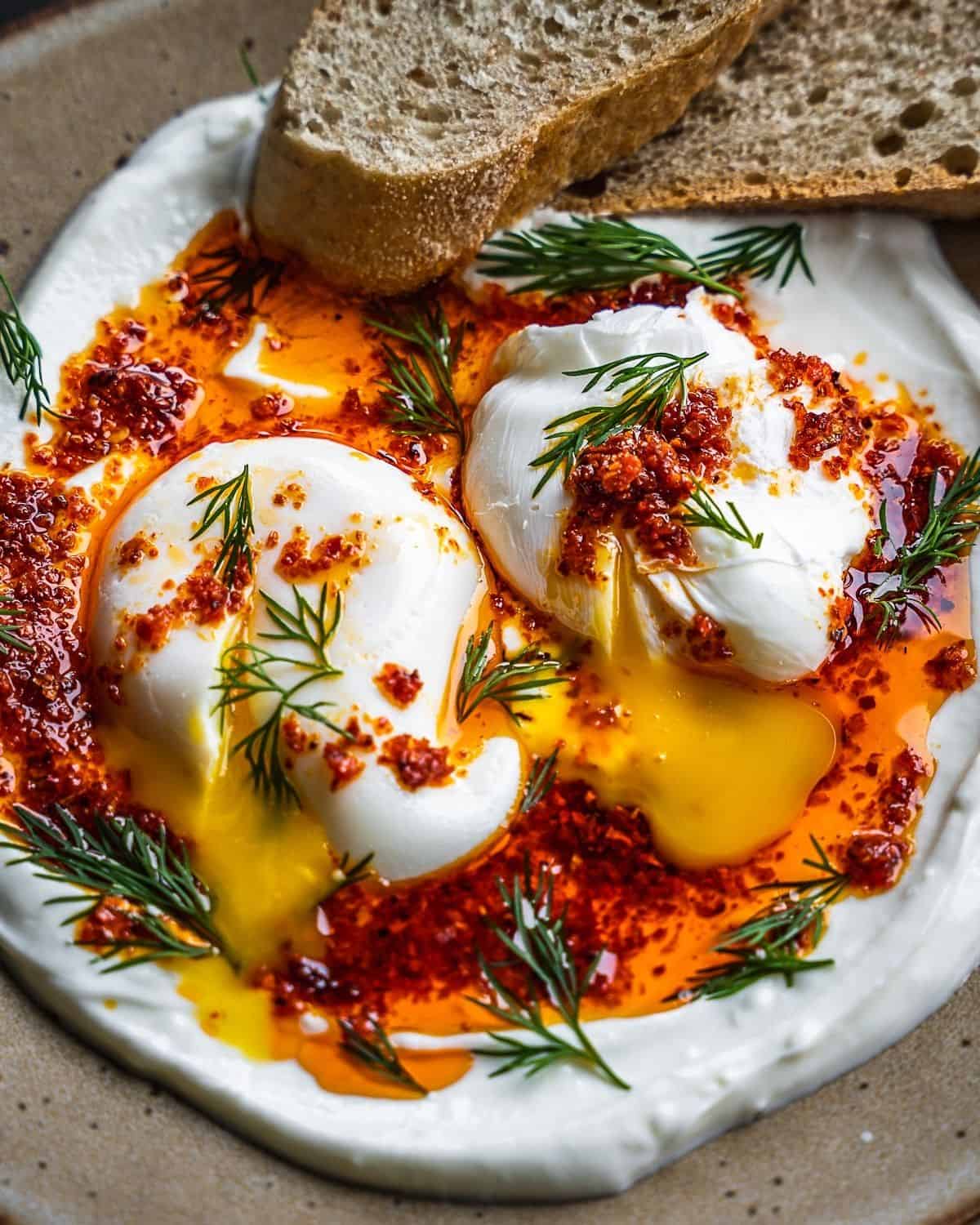 A beige plate with Turkish cilbir eggs and toast garnished with fresh dill.