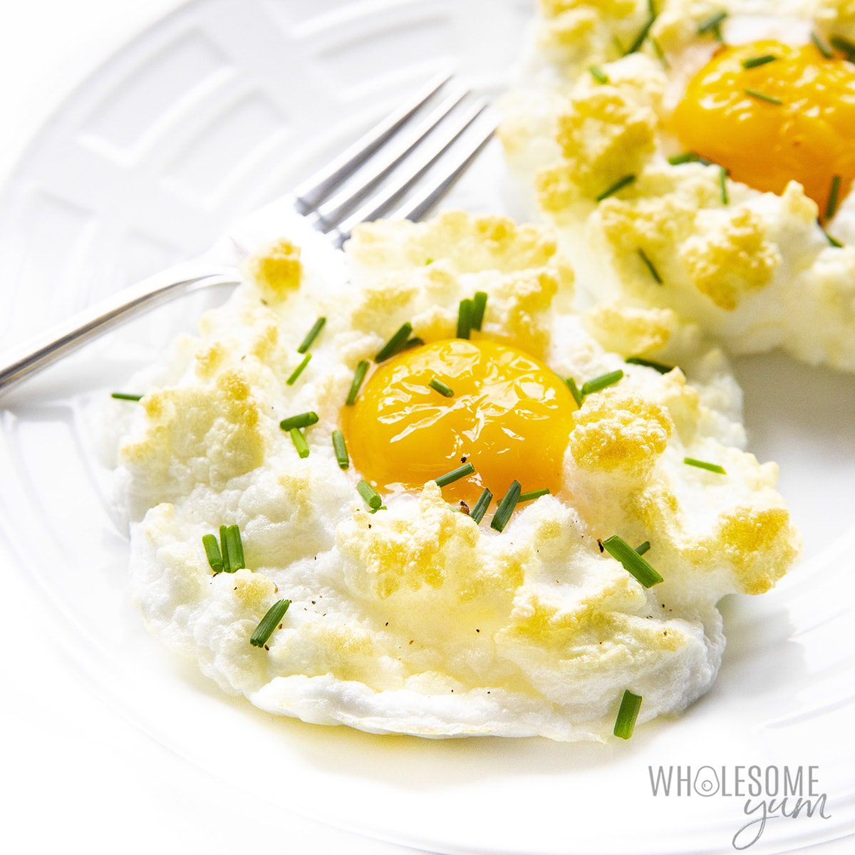 A white plate filled with cloud eggs, one of the 100 ways to cook an egg, with a fork and garnished with fresh chives.