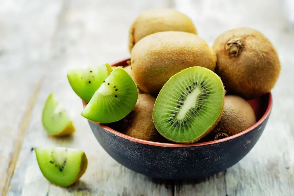 A vibrant bowl filled with whole kiwis and slices of the fruit, showcasing its bright green flesh dotted with tiny black seeds. Kiwi is a popular November seasonal produce in the USA, known for its high vitamin C content and tangy sweetness.