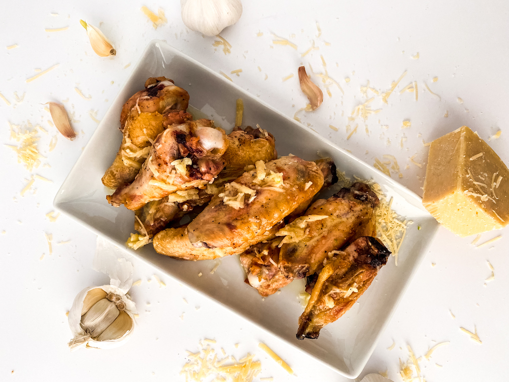 Garlic parmesan wings on a white plate sprinkled with freshly grated parmesan cheese.