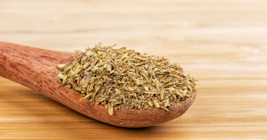 Dried oregano heaped in a wooden spoon on a bamboo cutting board