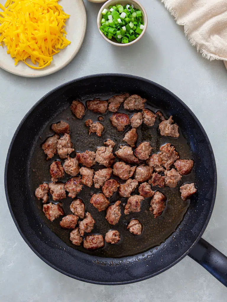 Potato Sausage Broccoli Breakfast Casserole Italian sausage being browned in a cast iron skillet for Potato Sausage Broccoli Breakfast Casserole.