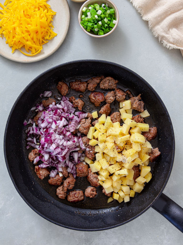 Red onion, potatoes and browned Italian sausage in a skillet.