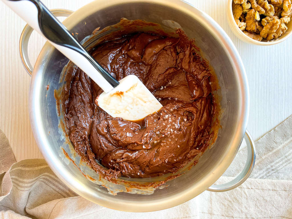 A spatula and melted chocolate in a sauce pan while adding the salt and vanilla extract to the chocolate walnut fudge.