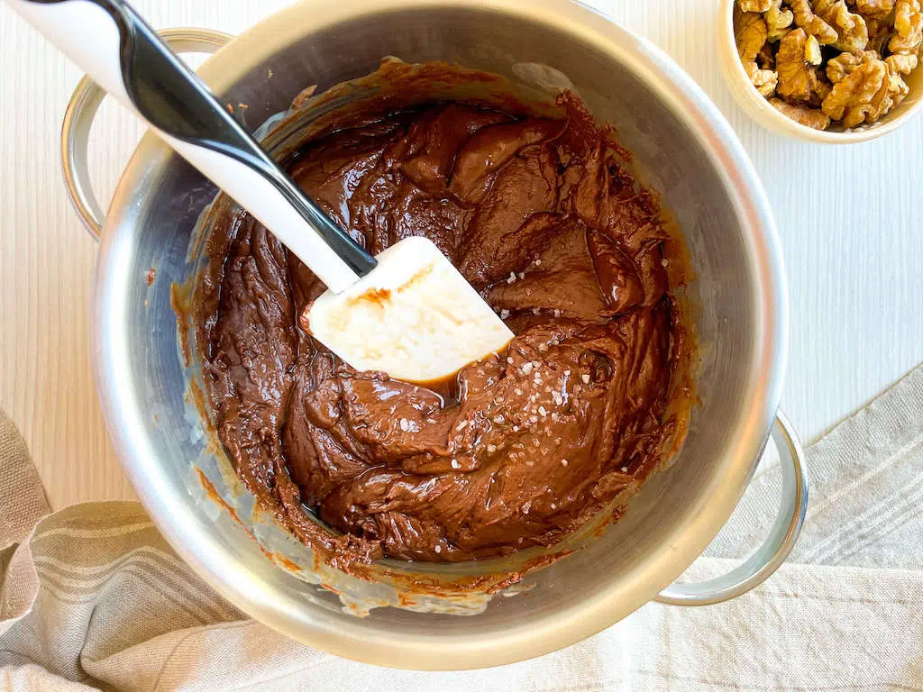 A spatula and melted chocolate in a sauce pan while adding the salt and vanilla extract to the chocolate walnut fudge.