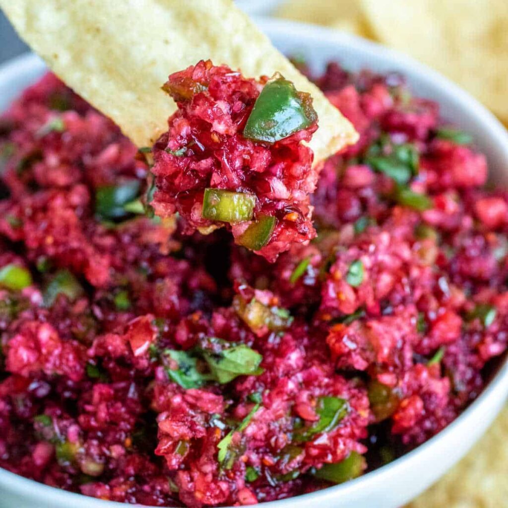 Tortilla chip dipping into chunky cranberry jalapeño salsa