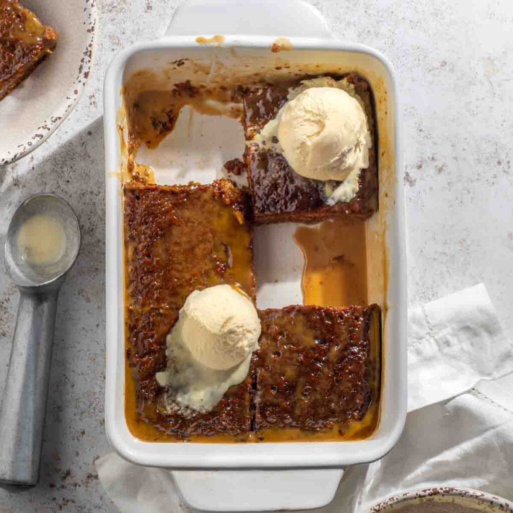 Sticky toffee pudding in baking dish with caramel sauce and vanilla ice cream