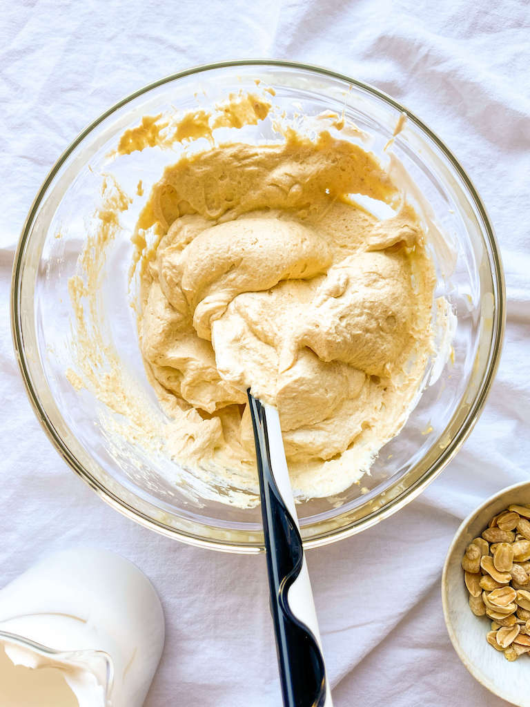 Peanut butter mousse with a spatula in a glass mixing bowl.