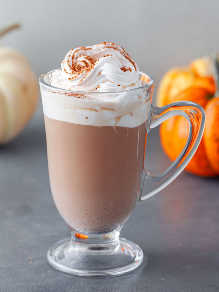 A glass mug of Pumpkin Spice Irish Coffee garnished with maple whipped cream and a sprinkle of pumpkin spice.
