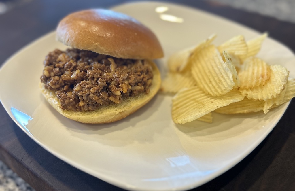 Sloppy Joe with Chicken Gumbo Soup on a white plate with potato chips on the side.