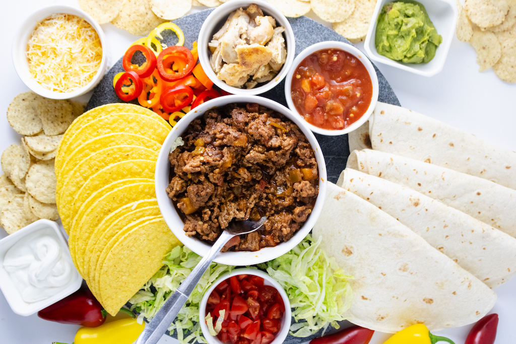 A Taco charcuterie board filled with taco meat, salsa, guacamole, tortillas and hard taco shells.