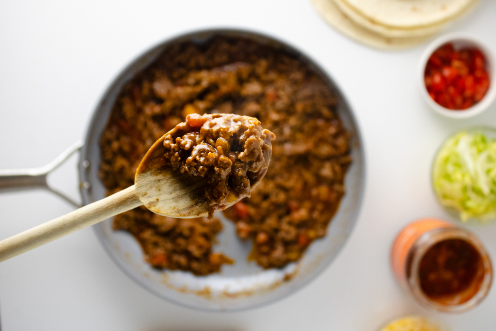 Scooping a spoonful of cooked taco meat out of a skillet.