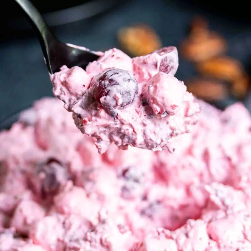 Close-up spoonful of cherry fluff salad, creamy pink dessert with cherries